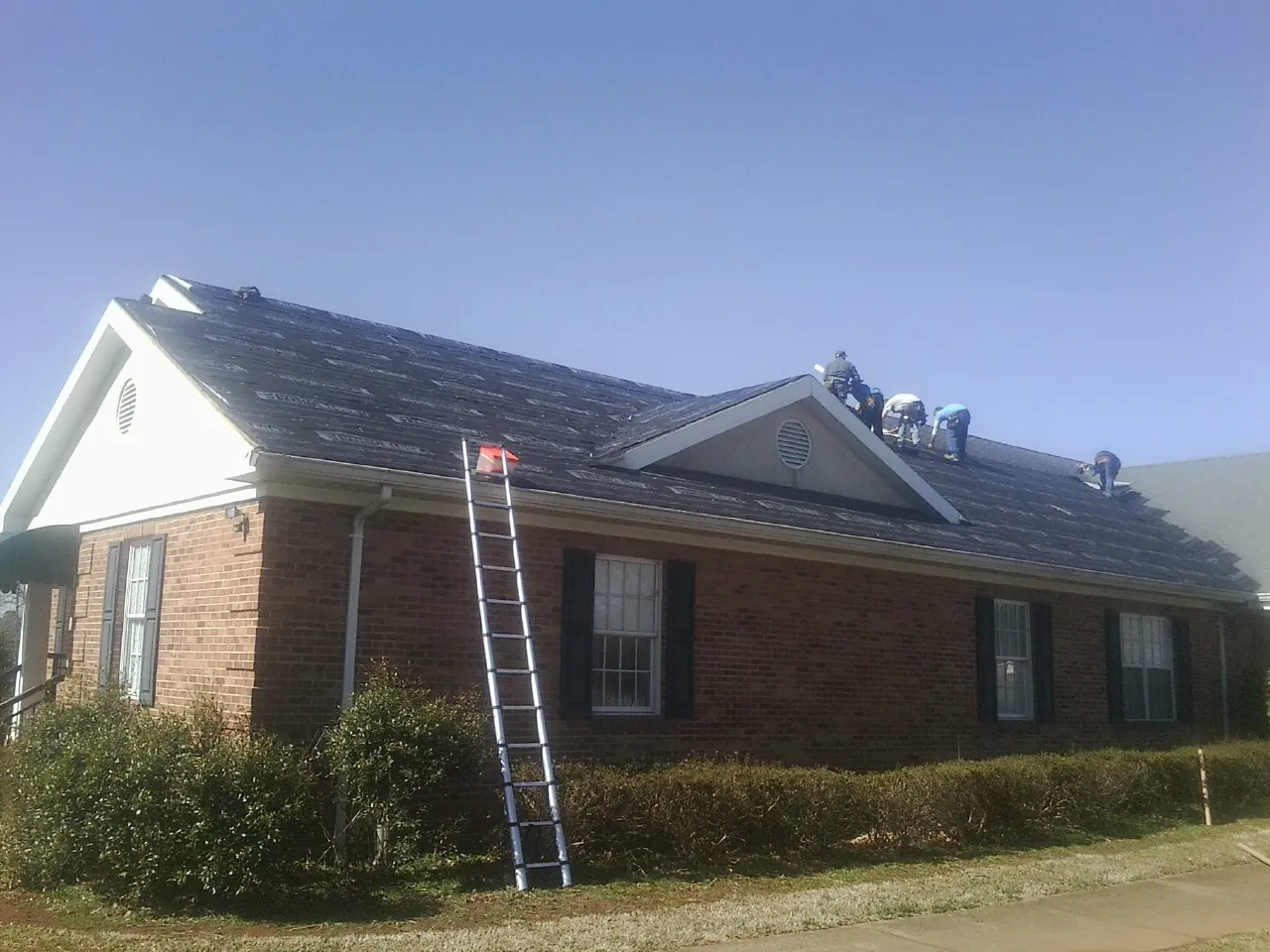 Crew tearing shingles off a brick ranch roof with a ladder set — Emergency Roof Repair work by our crew in Lithopolis