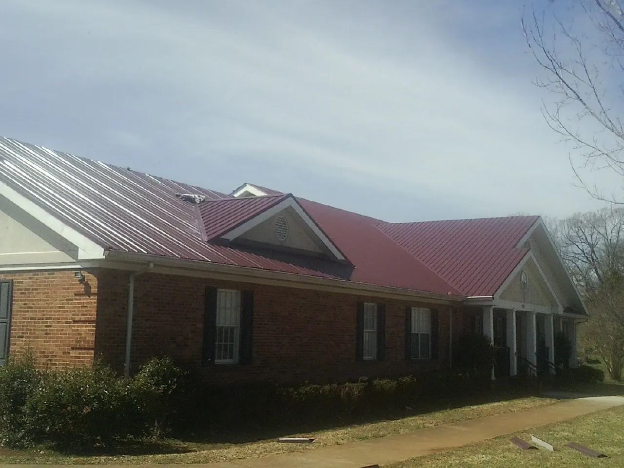 Red metal roof with gabled entries on a long brick building, from a Hail Damage Roof Repair job in Lithopolis
