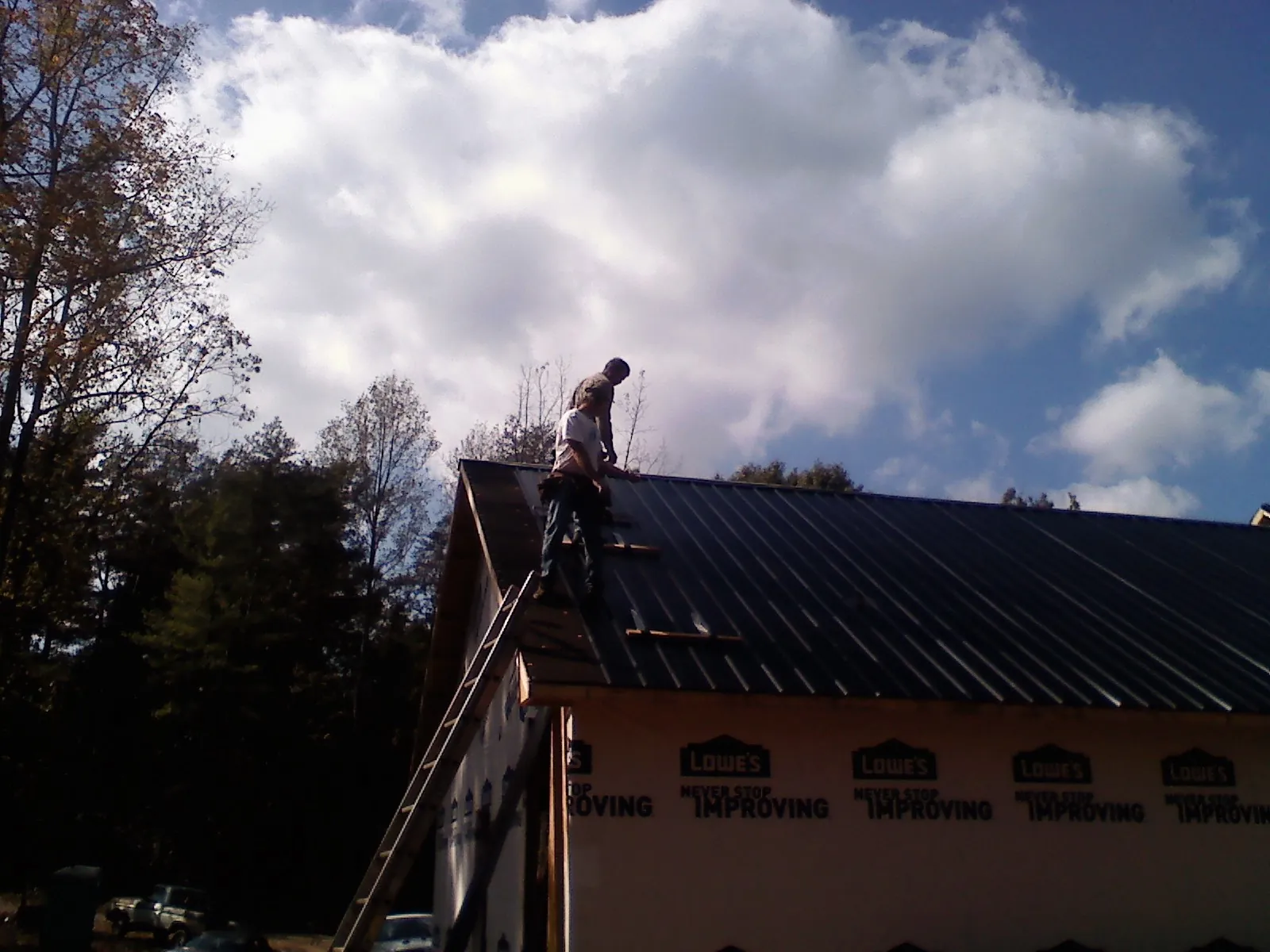 Roofer fastening dark metal panels high against a cloudy sky, from a Roof Inspection job in Lithopolis